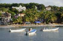 Mexico, Oaxaca, Puerto Escondido, Fishing boats in bay at Playa Marinero lined with cafes, bars and other buildings amongst palm trees.