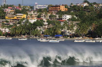 Mexico, Oaxaca, Puerto Escondido, Playa Principal, Breaking waves and boats overlooked by buildings amongst palm trees.