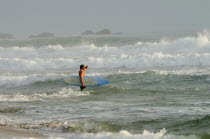 Mexico, Oaxaca, Puerto Escondidio, Surfer walking through surf carrying board.