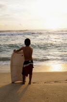 Mexico, Oaxaca, Puerto Escondido, Playa Zicatela, Young body boarder standing on beach looking out to sea.