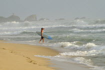 Mexico, Oaxaca, Puerto Escondido, Surfer walking into surf carrying board.
