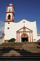 Mexico, Veracruz, Papantla, Cathedral de la Asuncion, white and red painted exterior facade and bell tower with flight of steps to entrance.