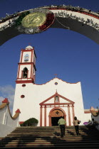 Mexico, Veracruz, Papantla, Cathedral de la Asuncion, white and red painted exterior, bell tower and steps to entrance framed by arch decorated for Independence Day celebrations.