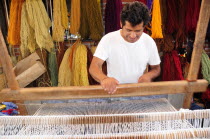 Mexico, Oaxaca, Teotitlan del Valle, Weaver at loom with different coloured yarn hanging in bundles behind.