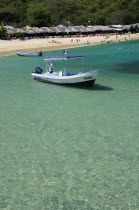 Mexico, Oaxaca, Huatulco, Playa La Entrega, Tour boat moored in clear,  shallow water in foreground of sandy beach lined with thatched, open fronted restaurants.