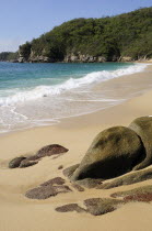 Mexico, Oaxaca, Huatulco, Bahia Chahue, Rocks and deserted, sandy beach with surf breaking on shore and rocky headland beyond.