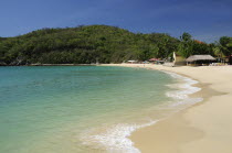 Mexico, Oaxaca, Huatulco, Sandy beach at Bahia Santa Cruz lined by restaurants and other buildings with tree covered coastline beyond.