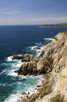 Mexico, Oaxaca, Huatulco, Rocky cliff edge with waves breaking on rocks below and Bahia Maguey.