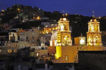 Mexico, Bajio, Guanajuato, Church of San Francisco at night with barrios on hillside beyond.
