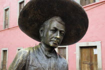 Mexico, Bajio, Guanajuato, Bronze statue of Charro singer Jorge Negrete with pink painted building facade behind.