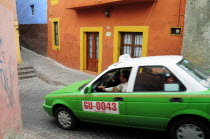 Mexico, Bajio, Guanajuato, Taxi turning down paved street with brightly painted corner houses.