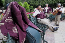 Mexico, Bajio, Guanajuato, Jardin de la Union, Mariachi group taking a rest from playing, purple jacket hung over music case in foreground.