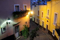 Mexico, Bajio, Guanajuato, Elevated view over street corner at night with painted building facades, balconies and illuminated street lights.