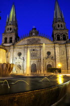 Mexico, Jalisco, Guadalajara, Fountain in foreground of cathedral exterior facade and bell towers at night in Plaza Guadalajara.