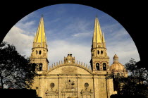 Mexico, Jalisco, Guadalajara, Plaza Guadalajara, Exterior facade of cathedral and bell towers framed by archway in shadow.