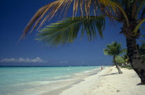 West Indies, Jamaica, Negril, sandy stretch of beach beside flat aquamarine water with woman walking along shoreline in distance.