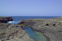 Cape Verde Islands, Island of Sal, Buracona, people climbing over rocky coast toward natural rock pool.