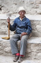 Nepal, Upper Mustang, Lo Manthang, elderly man praying with prayer wheel in the square near the king's palace.