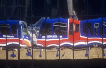 England, London, Docklands Light Railway train carriages reflected in glass of office building.