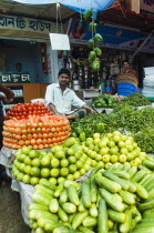 Bangladesh, Dhaka, Stall holder sat in market with neatly stacked piles of colourful vegetables around him.