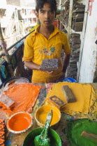 Bangladesh, Dhaka, Young man holding a printing block used to print on cotton fabrics in New Market with pallettes of colours in front of him.