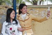 Vietnam, Two Young Ladies taking a picture of them selves, with a camera phone.