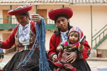 Peru, Mother and baby in traditional dress with a lady making yarn and infant holding mobile phone.
