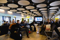 England, London, Heathrow Airport Terminal 5 disc ceiling in departures zone with passengers waiting in seating area at gate.