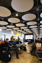 England, London, Heathrow Airport Terminal 5 disc ceiling in departures zone with passengers waiting in seating area at gate.