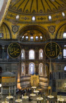 Turkey, Istanbul, Sultanahmet, Haghia Sophia Sighseeing tourists beneath the dome with murals and chandeliers in the Nave of the Cathedral with calligraphic roundels of Arabic Koran texts abobe the Lo...