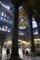 Turkey, Istanbul, Sultanahmet, Haghia Sophia Sighseeing tourists beneath the dome with murals and chandeliers in the Nave of the Cathedral.