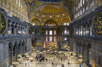 Turkey, Istanbul, Sultanahmet, Haghia Sophia Sighseeing tourists beneath the dome with murals and chandeliers in the Nave of the Cathedral.