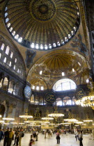 Turkey, Istanbul, Sultanahmet, Haghia Sophia Sighseeing tourists beneath the dome with murals and chandeliers in the Nave of the Cathedral.