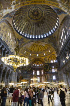 Turkey, Istanbul, Sultanahmet, Haghia Sophia Sighseeing tourists beneath the dome with murals and chandeliers in the Nave of the Cathedral.