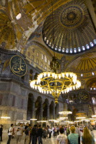 Turkey, Istanbul, Sultanahmet, Haghia Sophia Sighseeing tourists beneath the dome with murals and chandeliers in the Nave of the Cathedral.