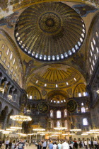 Turkey, Istanbul, Sultanahmet, Haghia Sophia Sighseeing tourists beneath the dome with murals and chandeliers in the Nave of the Cathedral.