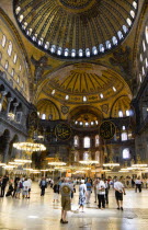 Turkey, Istanbul, Sultanahmet, Haghia Sophia Sighseeing tourists beneath the dome with murals and chandeliers in the Nave of the Cathedral.