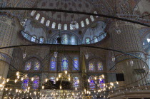 Turkey, Istanbul, Sultanahmet Camii, The Blue Mosque interior with decorated painted domes with chandelier below and stained glass windows beyond.