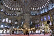 Turkey, Istanbul, Sultanahmet Camii, The Blue Mosque interior with people at prayer beneath chandeliers and decorated domes above and stained glass windows beyond.