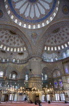 Turkey, Istanbul, Sultanahmet Camii, The Blue Mosque interior with people at prayer beneath chandeliers and decorated domes above and stained glass windows beyond.