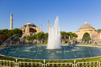 Turkey, Istanbul, Sultanahmet, Haghia Sophia with dome and minarets beyond the water fountain and Baths of Roxelana in the gardens with sightseeing tourists.