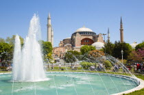 Turkey, Istanbul, Sultanahmet, Haghia Sophia with dome and minarets beyond the water fountain in the gardens with sightseeing tourists.