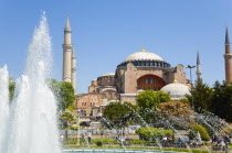 Turkey, Istanbul, Sultanahmet, Haghia Sophia with dome and minarets beyond the water fountain in the gardens with sightseeing tourists.