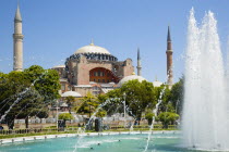 Turkey, Istanbul, Sultanahmet, Haghia Sophia with dome and minarets beyond the water fountain in the gardens with sightseeing tourists.