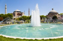 Turkey, Istanbul, Sultanahmet, Haghia Sophia with dome and minarets beyond the water fountain and Baths of Roxelana in the gardens with sightseeing tourists.