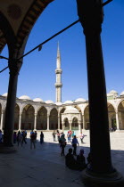 Turkey, Istanbul, Sultanahmet Camii, The Blue Mosque Courtyard and minaret with Absolutions Fountain in the middle and tourists walking in the shade under domed arches.