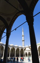 Turkey, Istanbul, Sultanahmet Camii, The Blue Mosque Courtyard and minaret with Absolutions Fountain in the middle and tourists walking in the shade under domed arches.