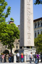 Turkey, Istanbul, Sultanahmet, Tourists in the Roman Hippodrome in At Meydani beside Egyptian Obelisk with Hieroglyphics from Luxor and relief at base showing Theodosius I and courtiers.