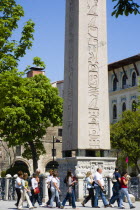 Turkey, Istanbul, Sultanahmet, Tourists in the Roman Hippodrome in At Meydani beside Egyptian Obelisk with Hieroglyphics from Luxor and relief at base showing Theodosius I and courtiers.