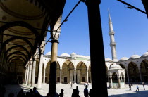 Turkey, Istanbul, Sultanahmet Camii, The Blue Mosque Courtyard and minaret with Absolutions Fountain in the middle and tourists walking in the shade under domed arches.